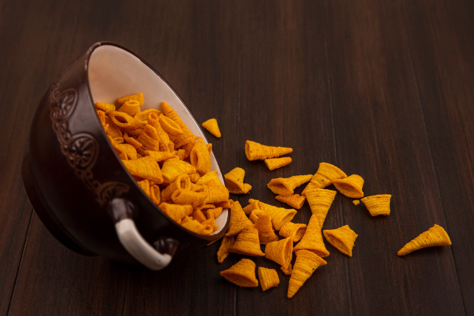 top view of tasty cone shape fried bugles chips falling out of a bowl on a wooden background